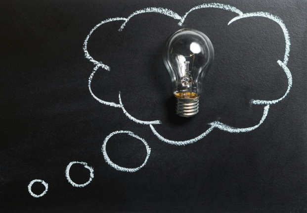 A lightbulb on a blackboard outlined in white chalk in a thought bubble cartoon.